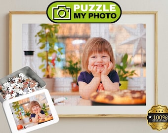 Könnte beinhalten: Ein individuelles Puzzle mit einem Foto eines lächelnden Kindes, das sein Kinn auf die Hände stützt. Das Puzzle ist in einem hellen Holzrahmen präsentiert, inklusive einer Metalldose mit losen Puzzleteilen und einem kleinen Referenzbild.