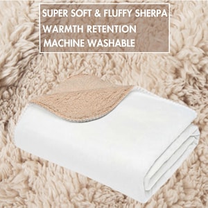 May include: A folded white blanket with a tan sherpa lining. The blanket is on a fluffy, tan surface. Text on the image reads: "SUPER SOFT & FLUFFY SHERPA, WARMTH RETENTION, MACHINE WASHABLE."