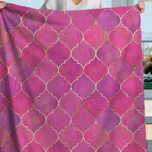May include: A pink and magenta blanket with a gold quatrefoil pattern. The blanket is held up, showcasing the design. The quatrefoil pattern is a repeating design of four overlapping circles, creating a decorative and elegant look.