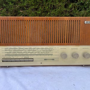 Może przedstawiać: Vintage radio Grundig z drewnianym panelem przednim i kremowym panelem sterowania. Radio posiada pokrętła i tarczę ze wskaźnikami stacji. Logo Grundig jest widoczne w prawym górnym rogu.