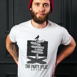 Può includere: Una t-shirt bianca con una grafica nera di un cartello stradale in legno con sopra un corvo. I cartelli indicano TAVERN, PLOT, SUSPICIOUS DOOR, BOAT e THE OTHER WAY. Sotto la grafica, il testo recita THE PARTY SPLIT. AGAIN. in lettere nere.