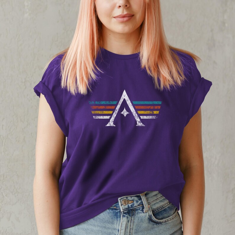A minimalist t-shirt featuring the Arcs board game logo in a retro style. The design includes white geometric lines with a central star and vintage-colored stripes (teal, orange, red, yellow) on a dark background. Perfect for board gamers, sci-fi fans, and anyone who loves stylish and unique game night apparel.