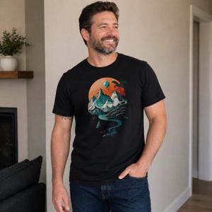 Man wearing the DnD mountain adventure shirt in black — vintage circular landscape design with snowy peaks, pine forest, D20, and soaring eagle in a relaxed indoor lifestyle setting