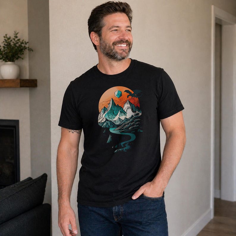 Man wearing the DnD mountain adventure shirt in black — vintage circular landscape design with snowy peaks, pine forest, D20, and soaring eagle in a relaxed indoor lifestyle setting