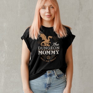 Dark red Dungeon Mommy T-shirt with a bold vintage-style dragon graphic above the phrase “Dungeon Mommy.” A large D20 dice and the words “Roll for Mercy” appear below, making this a funny and powerful gift for any Dungeons and Dragons fan. Ideal for gamer moms, dungeon masters, or fantasy lovers who want to show off their RPG pride in style. Perfect for birthdays, Mother’s Day, or any tabletop night.