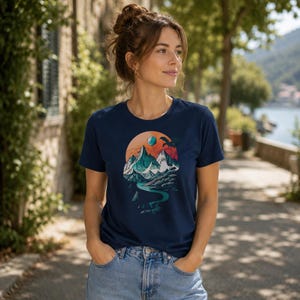 Woman wearing the DnD adventure mountain shirt in navy blue — outdoor waterfront lifestyle shot showing the vintage landscape circular print on a unisex everyday tee