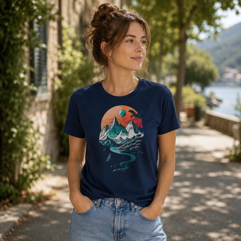 Woman wearing the DnD adventure mountain shirt in navy blue — outdoor waterfront lifestyle shot showing the vintage landscape circular print on a unisex everyday tee