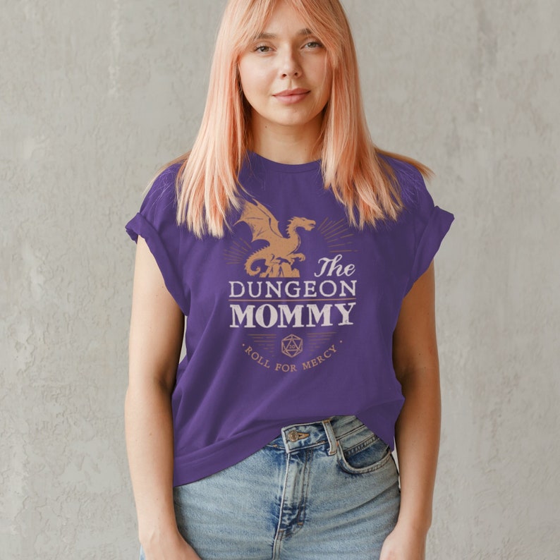 Dark red Dungeon Mommy T-shirt with a bold vintage-style dragon graphic above the phrase “Dungeon Mommy.” A large D20 dice and the words “Roll for Mercy” appear below, making this a funny and powerful gift for any Dungeons and Dragons fan. Ideal for gamer moms, dungeon masters, or fantasy lovers who want to show off their RPG pride in style. Perfect for birthdays, Mother’s Day, or any tabletop night.