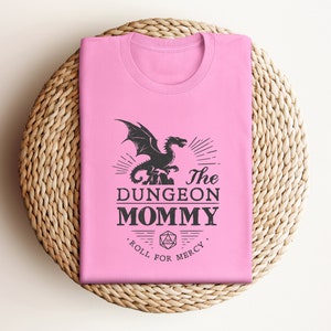 Dark red Dungeon Mommy T-shirt with a bold vintage-style dragon graphic above the phrase “Dungeon Mommy.” A large D20 dice and the words “Roll for Mercy” appear below, making this a funny and powerful gift for any Dungeons and Dragons fan. Ideal for gamer moms, dungeon masters, or fantasy lovers who want to show off their RPG pride in style. Perfect for birthdays, Mother’s Day, or any tabletop night.