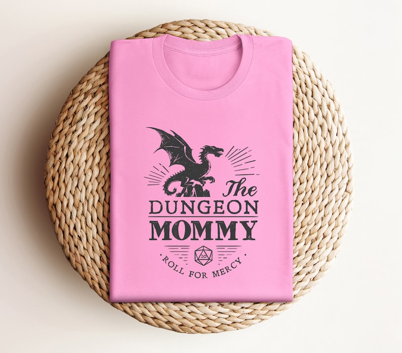 Dark red Dungeon Mommy T-shirt with a bold vintage-style dragon graphic above the phrase “Dungeon Mommy.” A large D20 dice and the words “Roll for Mercy” appear below, making this a funny and powerful gift for any Dungeons and Dragons fan. Ideal for gamer moms, dungeon masters, or fantasy lovers who want to show off their RPG pride in style. Perfect for birthdays, Mother’s Day, or any tabletop night.