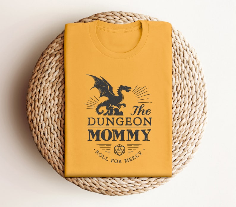 Dark red Dungeon Mommy T-shirt with a bold vintage-style dragon graphic above the phrase “Dungeon Mommy.” A large D20 dice and the words “Roll for Mercy” appear below, making this a funny and powerful gift for any Dungeons and Dragons fan. Ideal for gamer moms, dungeon masters, or fantasy lovers who want to show off their RPG pride in style. Perfect for birthdays, Mother’s Day, or any tabletop night.