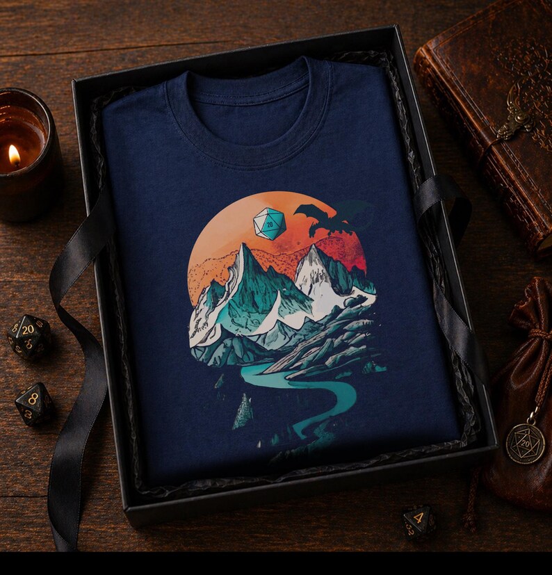 Navy DnD mountain adventure shirt folded in a dark moody gift box — vintage fantasy landscape design as a tabletop RPG gift for dungeon masters and outdoor adventure fans