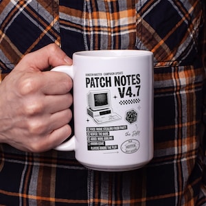 Könnte beinhalten: Ein weißer Keramikbecher mit schwarzem Aufdruck. Das Design zeigt einen alten Computer, einen zwanzigseitigen Würfel und den Text: Dungeon Master Campaign Update Patch Notes V4.7, Fixed: Rogue stealing from party, Nerfed: The Bard, Added: More Goblins, Known Issue: Players ignore the plot, the DM, sowie Hotfix V4.8 Next Session.