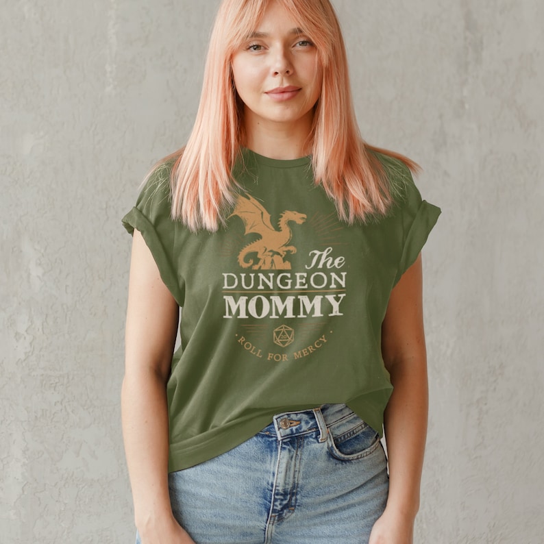 Dark red Dungeon Mommy T-shirt with a bold vintage-style dragon graphic above the phrase “Dungeon Mommy.” A large D20 dice and the words “Roll for Mercy” appear below, making this a funny and powerful gift for any Dungeons and Dragons fan. Ideal for gamer moms, dungeon masters, or fantasy lovers who want to show off their RPG pride in style. Perfect for birthdays, Mother’s Day, or any tabletop night.