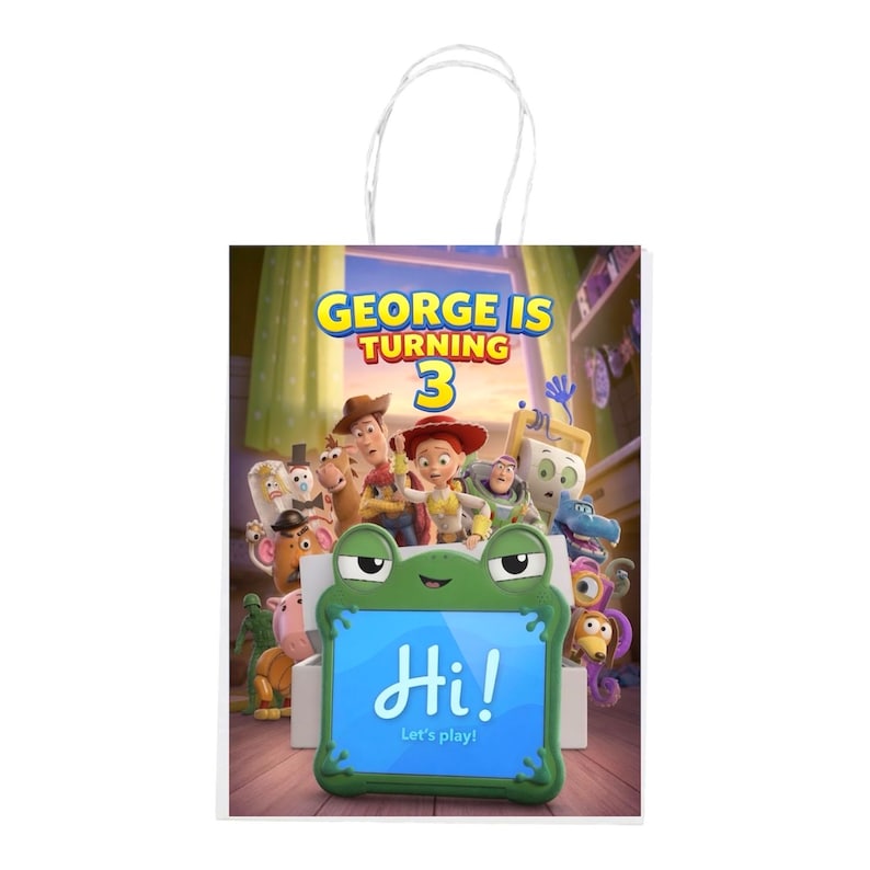 Pu&ograve; includere: Un sacchetto regalo in carta bianca con manico, decorato con personaggi di Toy Story, la scritta "GEORGE IS TURNING 3" e una cornice per tablet verde a forma di rana che mostra "Hi! Let's play!" su uno schermo blu in una stanza.