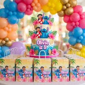 K&ouml;nnte beinhalten: Eine zweist&ouml;ckige Torte mit blauen Wellen, goldenen Palmbl&auml;ttern, rosa Hibiskusbl&uuml;ten und Lilo und Stitch Figuren. Die Torte tr&auml;gt die Aufschrift Olivia is 8. Davor stehen mehrere Geschenkt&uuml;ten mit dem gleichen Lilo und Stitch Motiv.