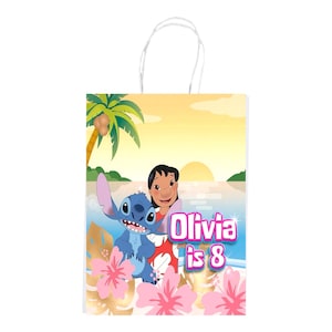 K&ouml;nnte beinhalten: Eine Geschenkt&uuml;te aus Papier mit wei&szlig;en gedrehten Papiergriffen, die eine tropische Sonnenuntergangsszene mit einer Palme, Lilo und Stitch zeigt. Der Text Olivia is 8 ist in rosa und wei&szlig;er Schrift gedruckt. Rosa Hibiskusbl&uuml;ten verzieren den unteren Bereich.