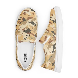 Puede incluir: Un par de zapatos de lona blancos sin cordones con un patrón de camuflaje en tonos marrones, beige y verdes. Los zapatos tienen la palabra "REBURN" impresa en el interior.