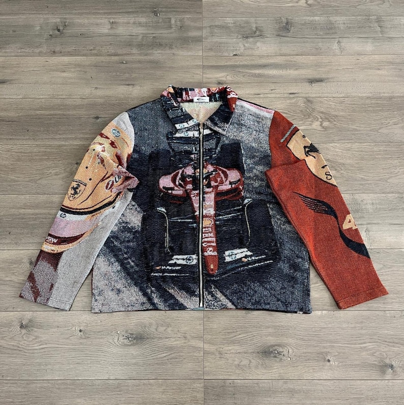 May include: A tapestry jacket with a full-length zipper. The jacket features a design with a race car and the Ferrari logo. The color palette includes shades of gray, red, beige, and black.