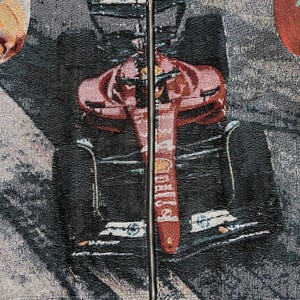 May include: A tapestry featuring a Formula 1 race car in red and black. The car's design is detailed, with the word "Shell" visible on the front. The background is a mix of gray and black, with a zipper running down the center.