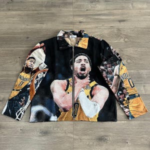May include: Black zip-up jacket with a basketball player in a yellow and black uniform. The jacket has a collared neckline and a full-length zip. The design includes images of the player in action, with the word "INDIANA" visible.