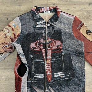 May include: A tapestry jacket with a full-length zipper and a collared neckline. The jacket features a Formula 1 race car design in shades of red, black, and gray. The sleeves and back panels have additional abstract patterns and colors.