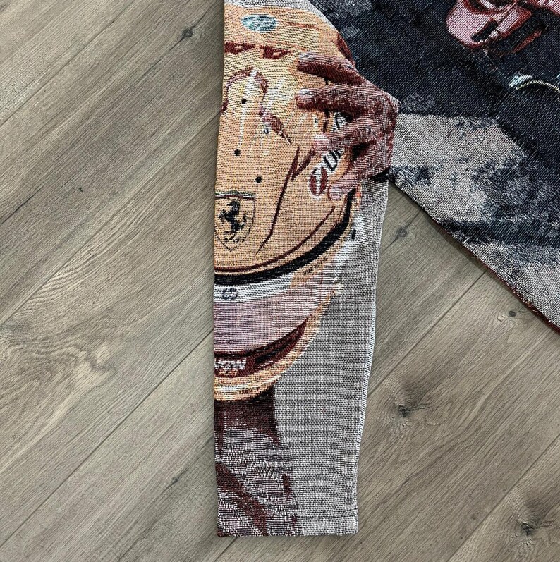 May include: Tapestry featuring a detailed image of a racing helmet with the Ferrari logo. The helmet is primarily tan with black and white accents. The tapestry is made of woven fabric and has a textured appearance.