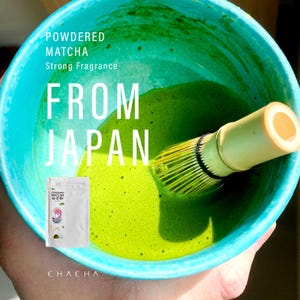 以下が含まれることがあります： 鮮やかな緑色の抹茶が、ターコイズブルーのボウルの中で泡立てられています。「Powdered Matcha, Strong Fragrance, From Japan」の文字が表示されています。抹茶パウダーの小さなパックが見えます。
