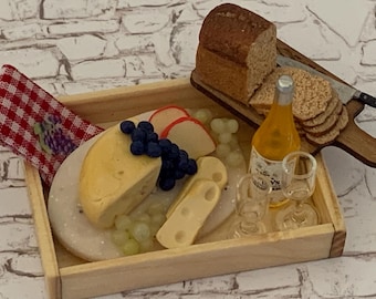 Puede incluir: Arreglo de comida en miniatura en una bandeja de madera. Incluye una cuña de queso amarillo, uvas, fruta en rodajas, galletas saladas, pan y una botella de líquido con dos vasos pequeños. También se incluye una servilleta a cuadros rojos y blancos.