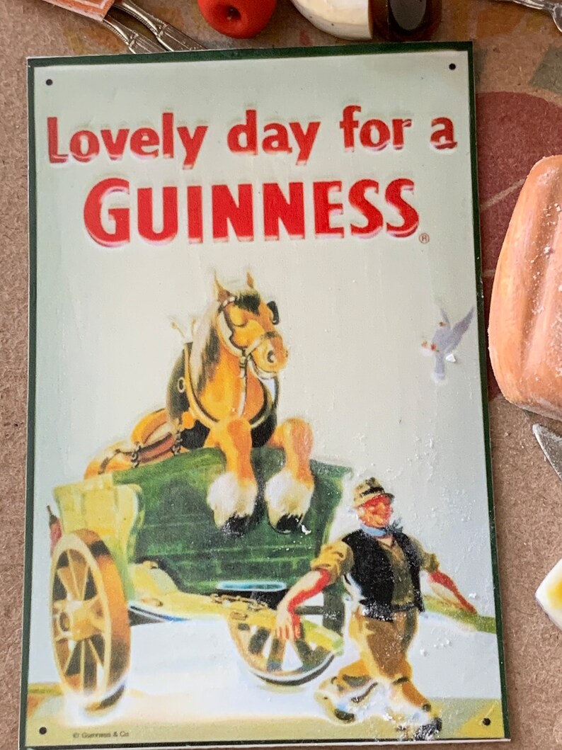May include: A vintage metal sign with a green border and white background. The sign features a red and white illustration of a horse pulling a cart. The text on the sign reads "Lovely day for a GUINNESS".