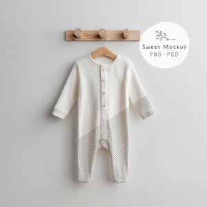 Peut inclure: Combinaison pour bébé crème à manches longues et fermeture boutonnée. La moitié inférieure de la combinaison présente un motif à carreaux gris et blanc. Le vêtement est suspendu à un cintre en bois sur un mur blanc.