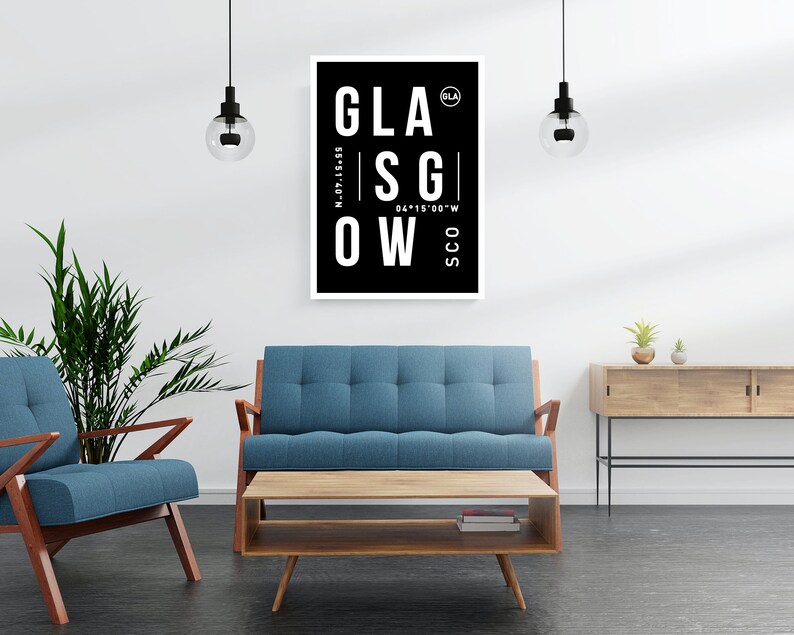 May include: A black and white poster with the word "GLASGOW" in large white letters. The poster also includes the coordinates "N-55.87.15.55" and "W 04.15.00.00". The poster is hanging on a white wall in a living room setting with a blue sofa, a coffee table, and a plant.