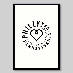May include: Black and white graphic design with the word "Philly" in a circle around a heart shape. The text "Pennsylvania" is written in a circle around the word "Philly". The coordinates 39.57'10"N and 75.09'49"W are written in smaller text around the heart.