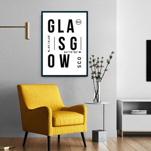 May include: A black and white poster with the word "GLASGOW" in large, bold letters. The poster also includes the coordinates "55&deg;51&prime;40&Prime;N 04&deg;15&prime;00&Prime;W" and the abbreviation "SCO" for Scotland. The poster is framed in a black frame and is hanging on a white wall.