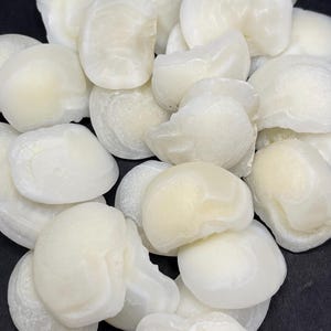May include: A pile of off-white, smooth, shell-shaped objects. The objects have a slightly translucent appearance and a subtle, creamy hue. The shapes are irregular, with rounded edges and a slightly textured surface. The objects are arranged closely together.