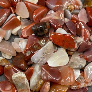 May include: A collection of polished gemstones in shades of red, orange, and white. The stones vary in size and shape, with smooth, rounded surfaces. Some stones have unique patterns and inclusions, creating a natural, earthy aesthetic. Ideal for jewelry making or collecting.