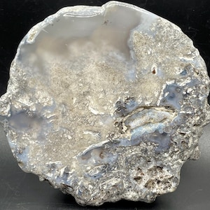 May include: A polished, irregularly shaped agate stone with a mix of gray, white, and blue hues. The stone has a rough, textured exterior and a smooth, polished interior, showcasing natural patterns and variations. A unique decorative item.