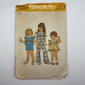 May include: Vintage Simplicity sewing pattern 7554, size 2. The pattern features illustrations of three young children in different outfits: a blue top and shorts, plaid pants and top, and a yellow floral dress. The pattern envelope is aged with wear.