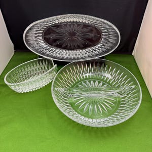 May include: A set of three clear glass serving dishes with a diamond pattern. The dishes are a large oval platter, a round bowl with a divider, and a smaller oval bowl.