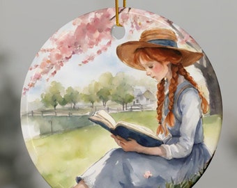Op de afbeelding: Een ronde keramische ornament met een aquarel-illustratie van een meisje met rood haar dat onder een bloeiende boom zit en een boek leest.
