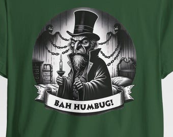 Könnte beinhalten: Dunkelgrünes T-Shirt mit einer Schwarz-Weiß-Illustration eines Mannes mit Zylinder, der eine Kerze hält. Der Text "BAH HUMBUG!" ist auf einem Banner zu sehen, mit Geisterfiguren im Hintergrund.