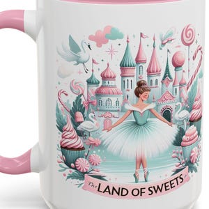 May include: White ceramic mug with a pink handle and interior. The mug features a whimsical illustration of a ballerina in front of a candy-themed castle. The text "The Land of Sweets" is printed on the mug.