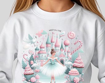 Op de afbeelding: Witte sweatshirt met een grillige illustratie van een ballerina voor een snoepkasteel. Het ontwerp bevat cupcakes, lolly's en de tekst "LAND OF SWEETS". De sweatshirt wordt gedragen door een persoon met hartvormige zonnebrillen.