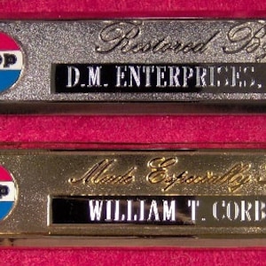 Puede incluir: Dos placas rectangulares, una plateada y otra dorada, con el logotipo de Jeep y texto. La placa superior dice "Restaurado por D.M. ENTERPRISES, INC." La placa inferior dice "Hecho especialmente para WILLIAM T. CORBIN".