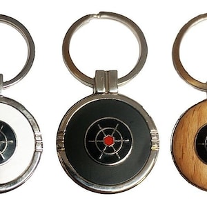 May include: Three keyrings with circular pendants. Each pendant has a target design with a red centre and black and silver accents. One has a white background, one is black, and the third is wood-toned. The rings are silver-coloured.