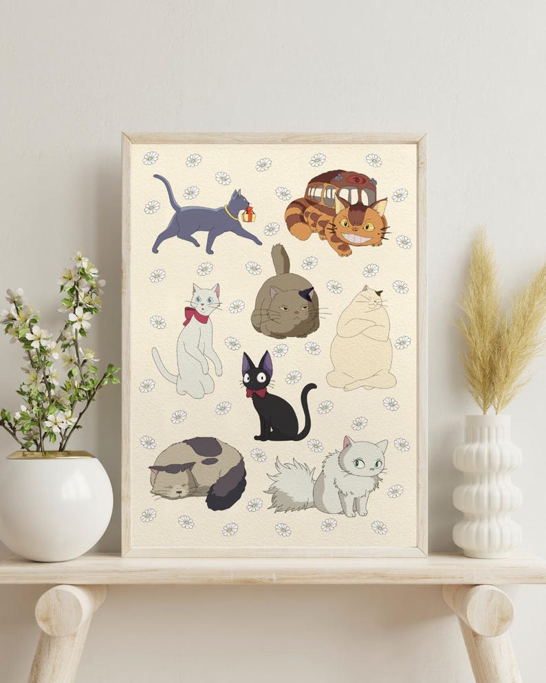 May include: A framed print featuring cartoon cats in various poses and colors. The cats are set against a cream-colored background with small white flower illustrations. The print is displayed on a light-colored wooden shelf.
