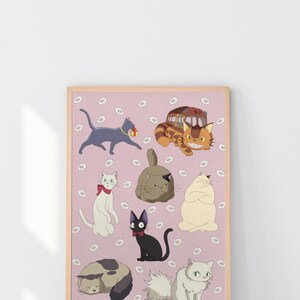 May include: A framed print featuring cartoon cats in various poses on a pink background with white flower accents. The cats are in different colors, including gray, black, white, and tan. The print has a light brown frame.
