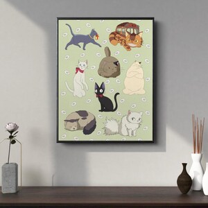 May include: A framed print featuring cartoon cats on a light green background with white daisy accents. The cats are in various poses and colors, including gray, white, black, and orange. The print has a black frame and is displayed on a dark wooden surface.