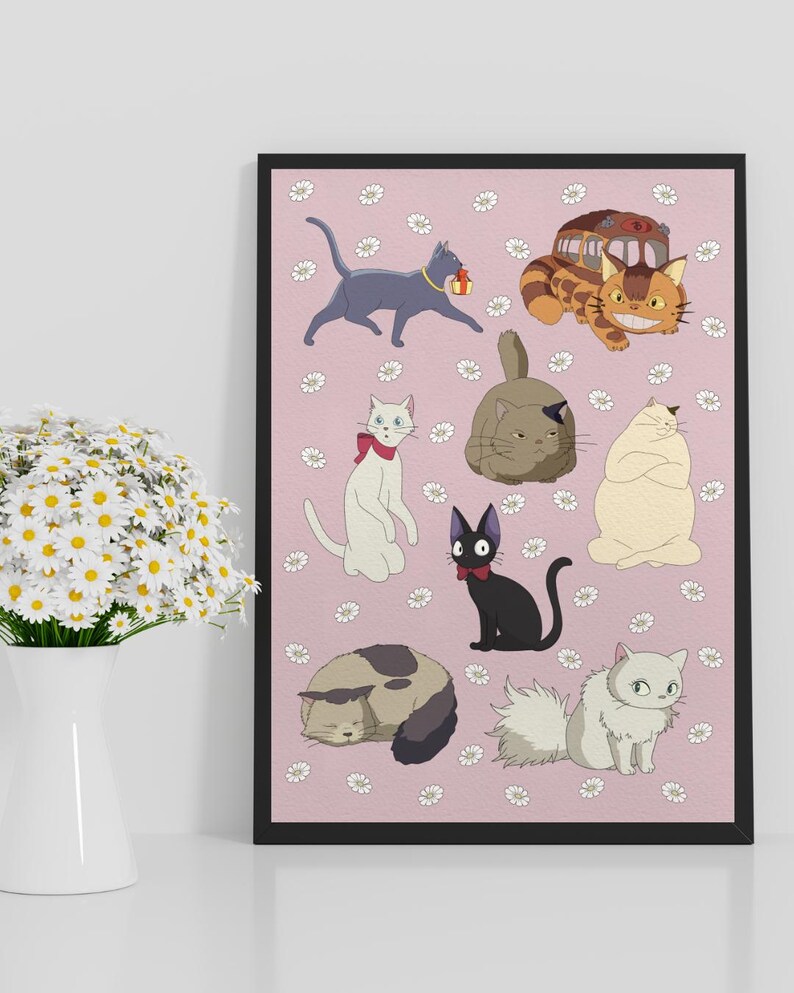 May include: A framed print featuring cartoon cats in various poses on a pink background with white daisy accents. The cats are in different colors, including gray, white, black, and tan. The print is displayed on a white surface.