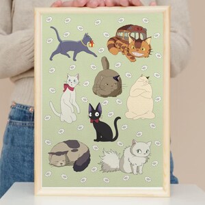 May include: A framed print featuring cartoon cats in various poses on a light green background with white flower accents. The cats are in different colors, including gray, black, white, and brown. The frame is a light wood color.